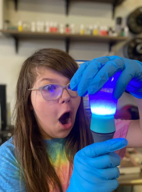 A student in safety gloves gasps at a glowing blue experiment in science class